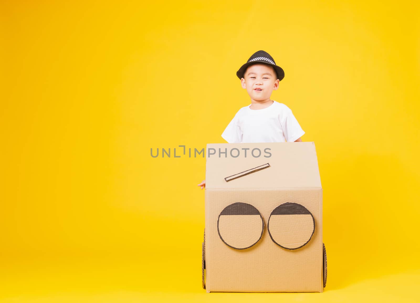 Portrait happy Asian cute little children boy smile so happy wearing white T-shirt driving car creative by cardboard, studio shot on yellow background with copy space
