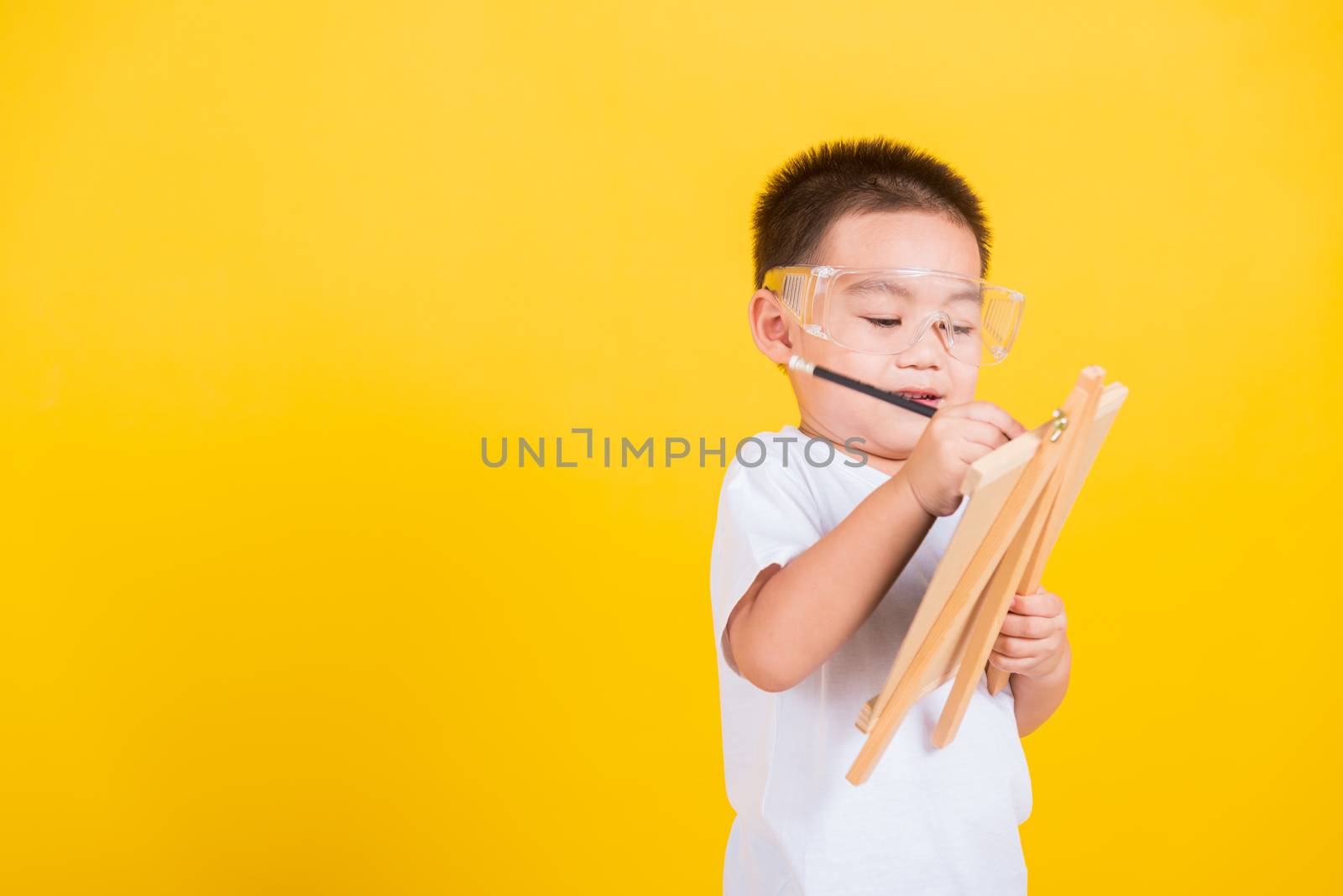 Asian Thai happy portrait cute little cheerful child boy smile are drawing on blackboard and looking the board, studio shot isolated on yellow background with copy space