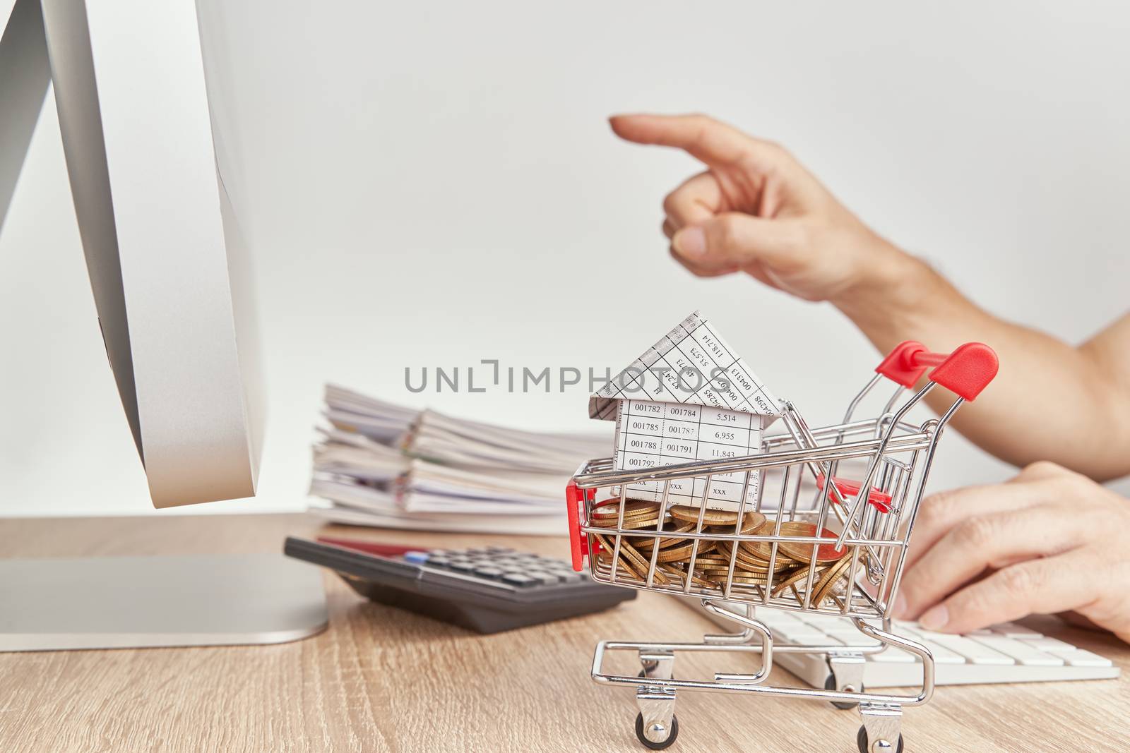 House on gold coins in shopping cart have blur man pointing finger for checking sales of shopping online concept and pile report of sale on wooden computer table with white background and copy space.