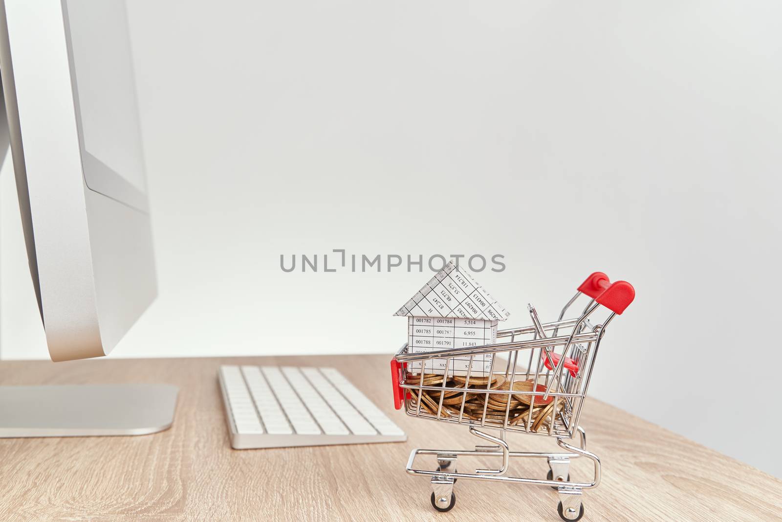 House on gold coins in shopping cart on wooden computer table with white background and copy space. Business and finance concepts shopping online photography.
