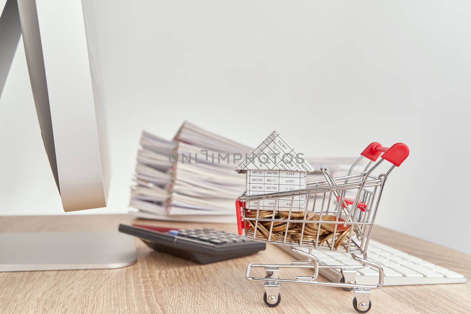 House on gold coins in shopping cart have blur calculator with pencil and pile report of sale on wooden computer table with white background and copy space. Business concepts shopping online.