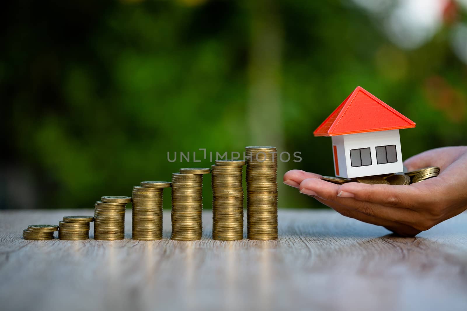 Orange roof house in investor's hand Placed close to the medallion, increasing the number of coins. Real estate investment concept, saving and buying houses, mortgage and bank loans.