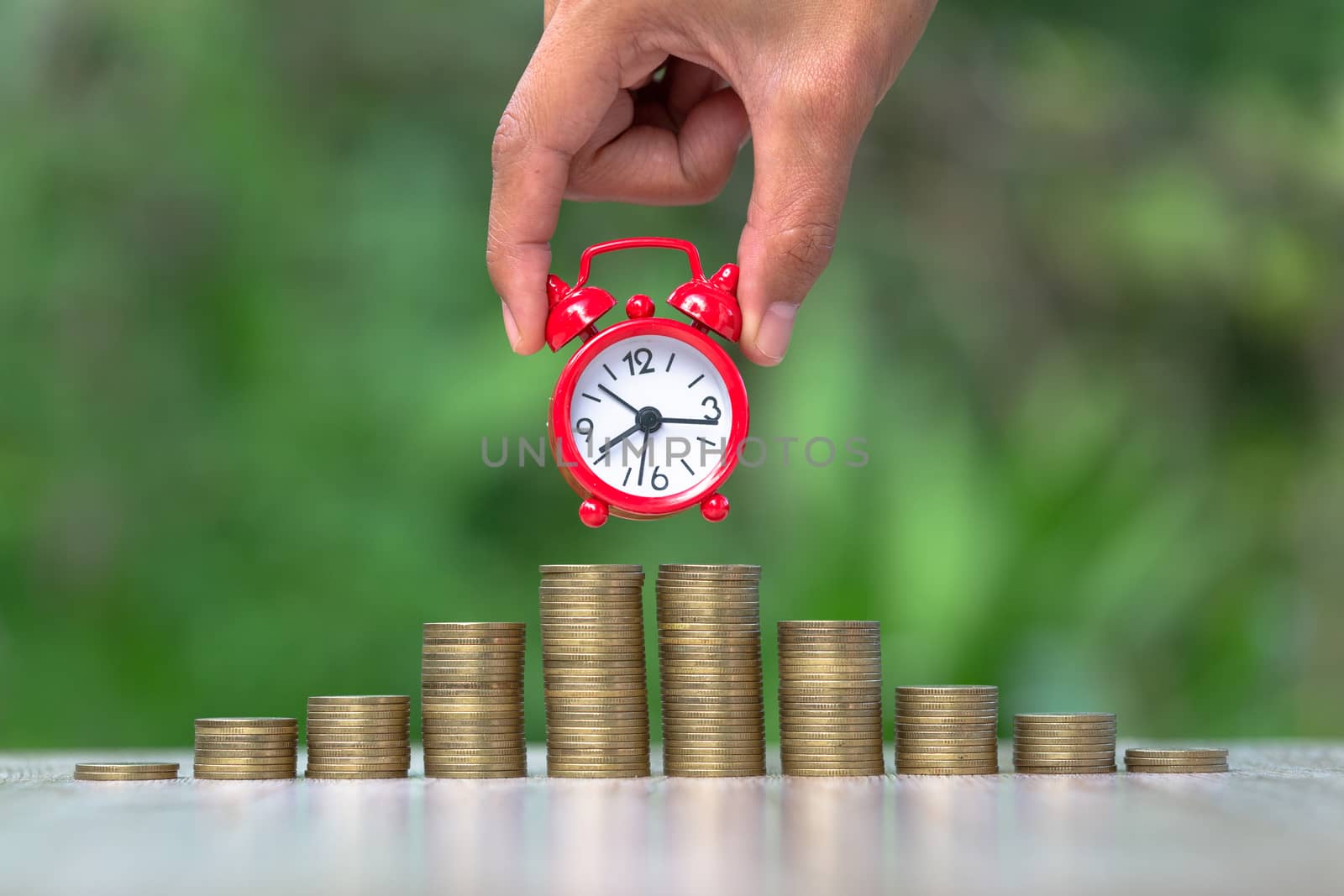 A red clock on a pile of coins.Red alarm clock Put on the coin ladder Ideas to save money, investment, business growth ideas, use the right time to invest.The idea of using time to be worth the money.