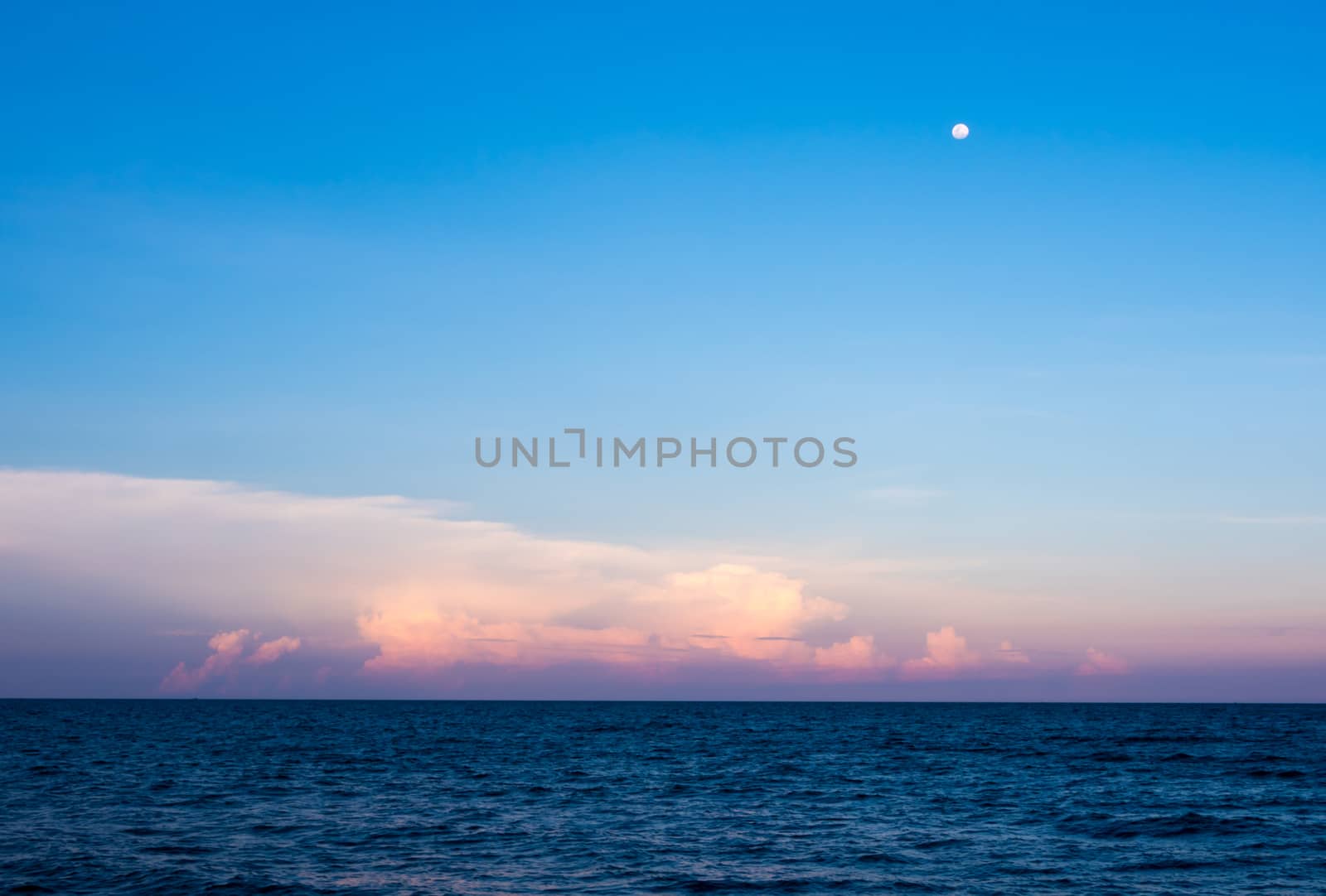 Pink Clouds and moon in sunset sky over sea