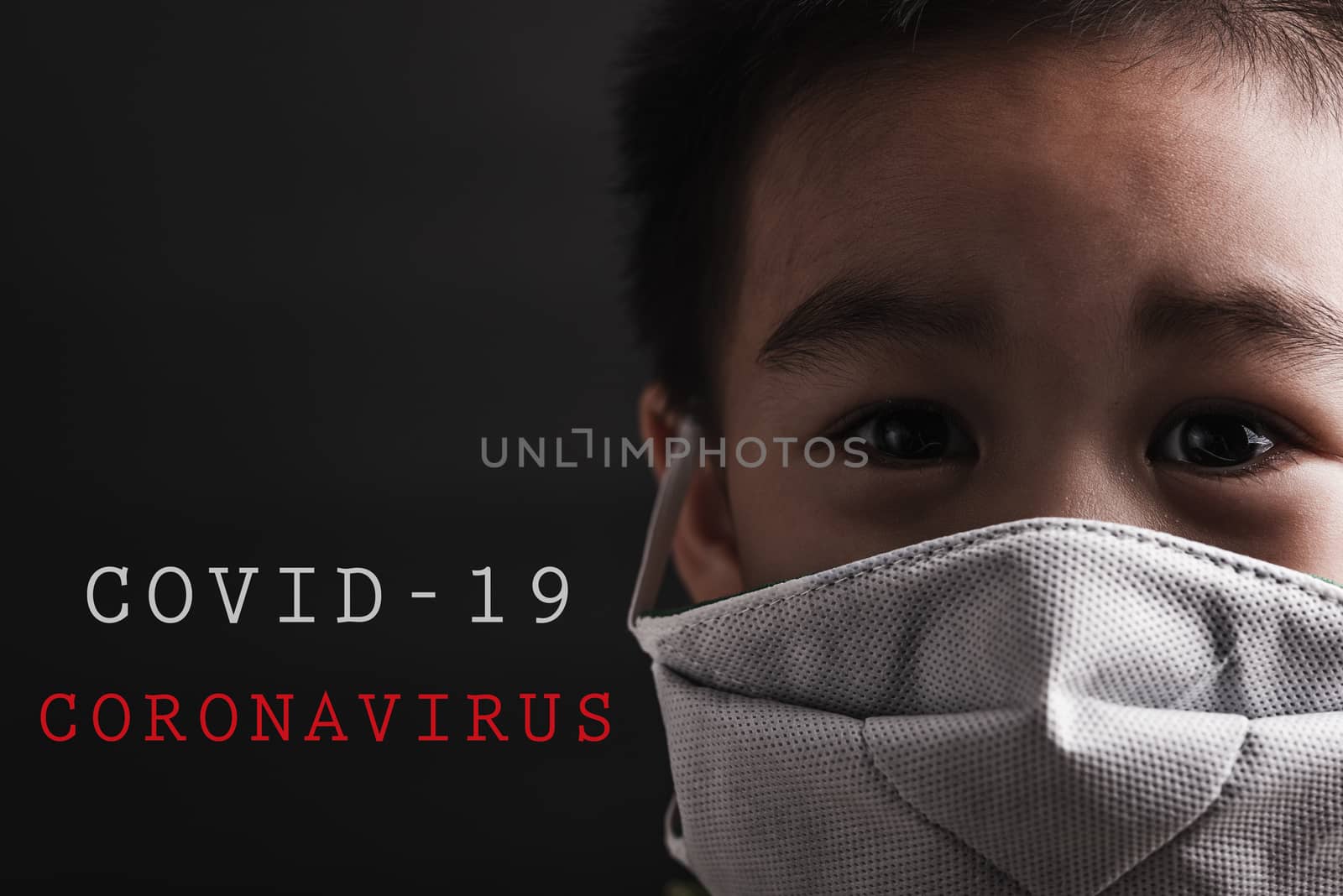 Closeup Asian little child wearing protective face mask with fear in the eye, prevent germs or disease hygiene prevention COVID-19 virus or coronavirus protection concept, dark on black background