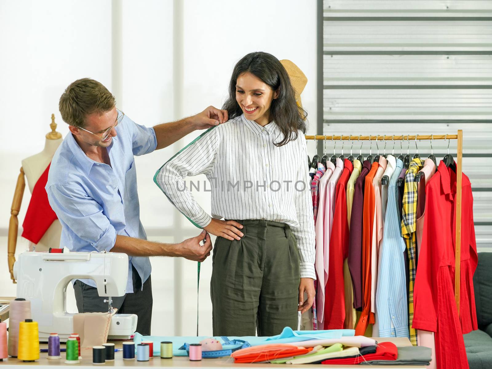 Fashion designer room, man and woman working in home base cloth design business. Men's tailors are measuring the length from the shoulders, elbows to the wrists of young customers.