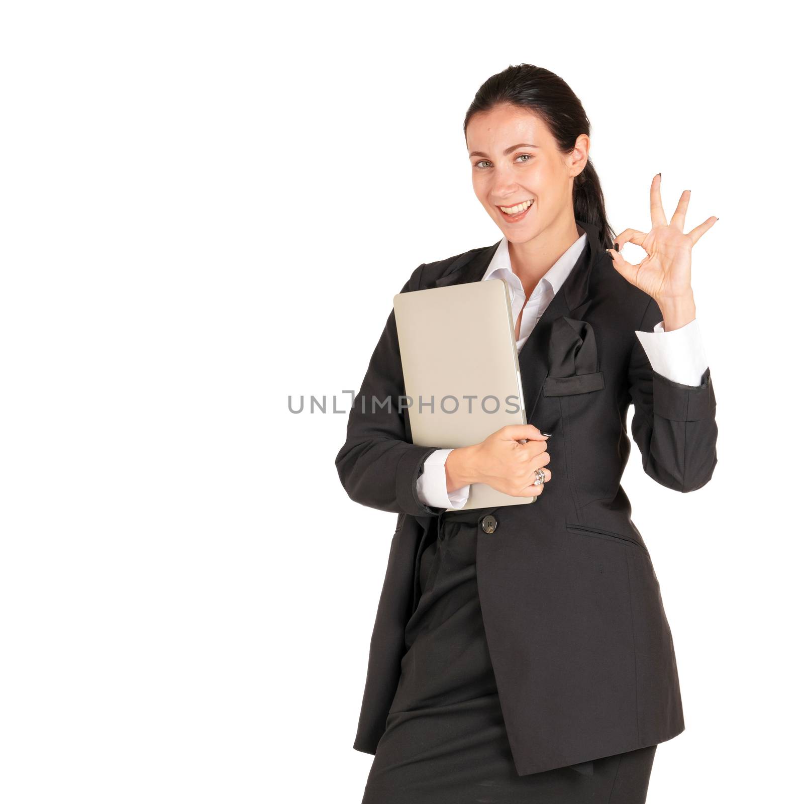 A business woman in a black suit with a finger, symbolizing okay, carrying a laptop computer. Portrait on white background with studio light.