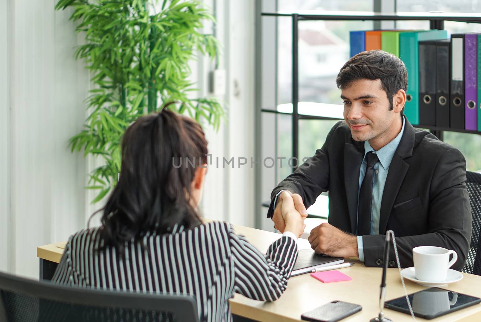 Young employers in black suits shaking hands during a meeting in the office. Pleasant atmosphere after a job interview.