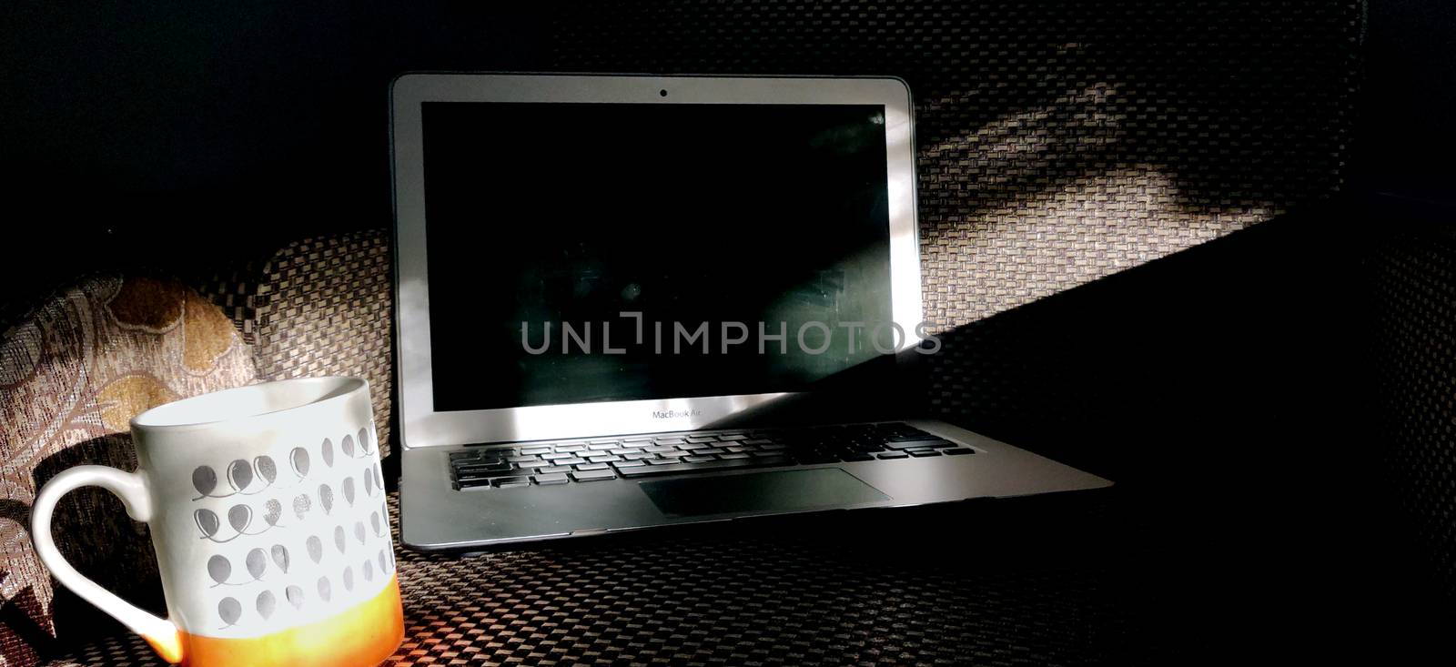 Screen of a laptop kept on the couch with a steaming cup of coffee basking in the rays of sun in the morning