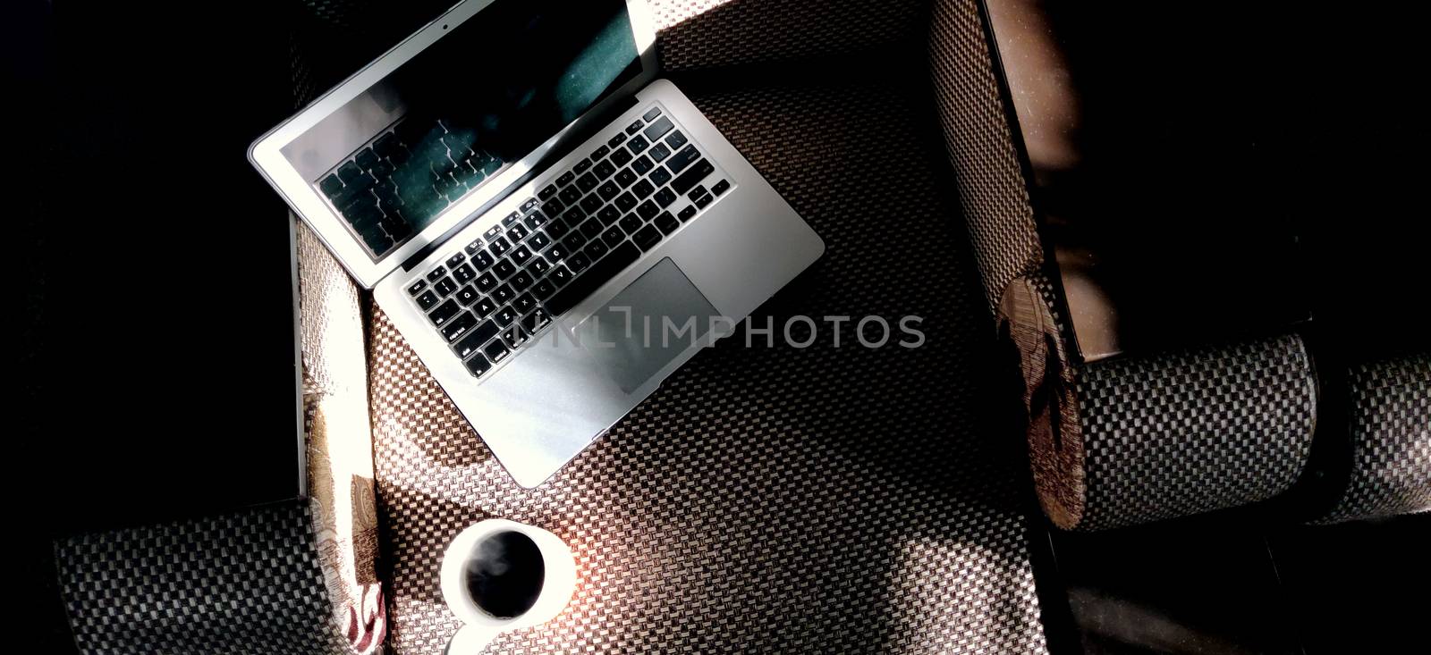 Laptop and mug of steaming coffee on the couch in the light of the morning sun