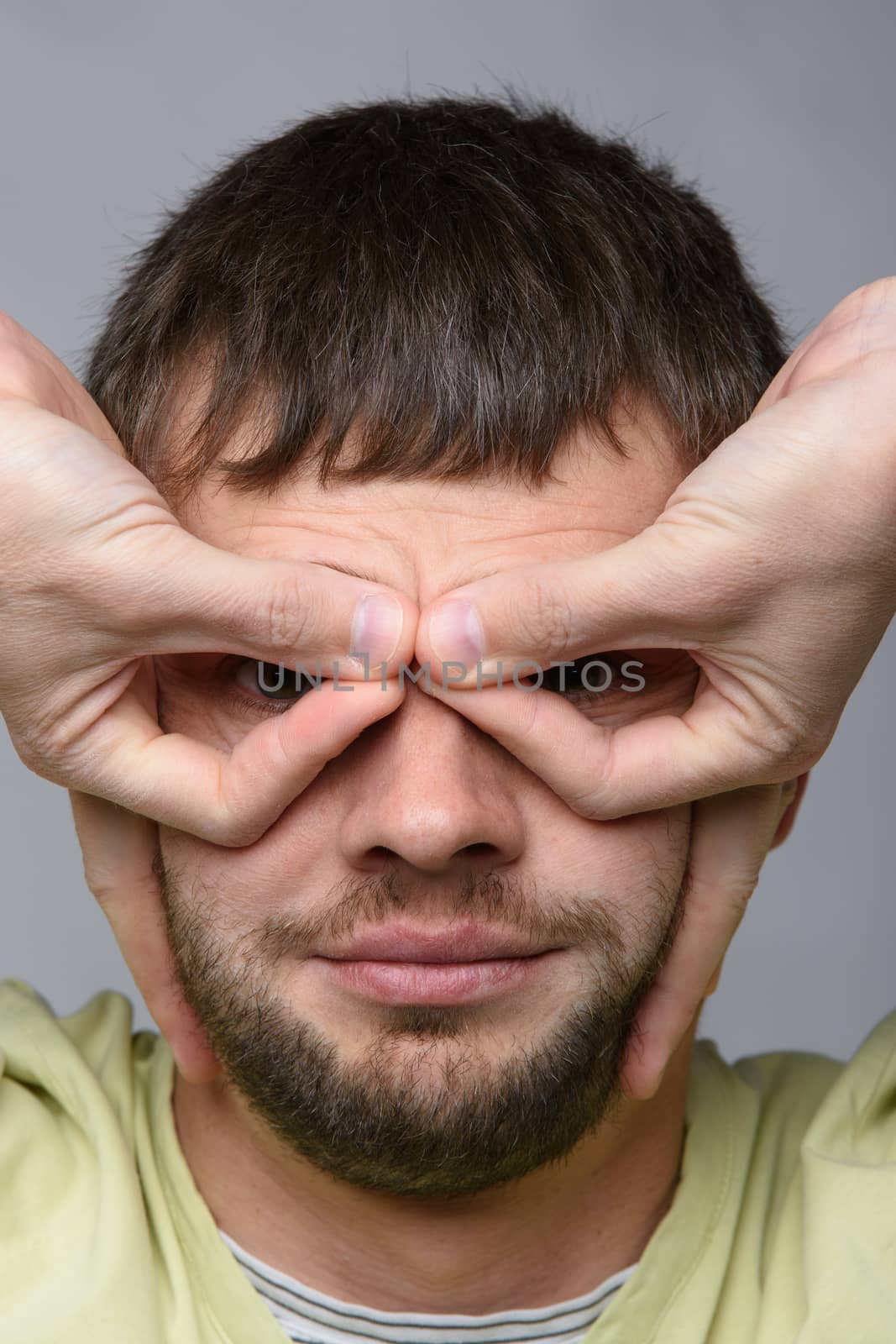 Close-up portrait of a man who made with his hands a kind of glasses on the eyes of European appearance