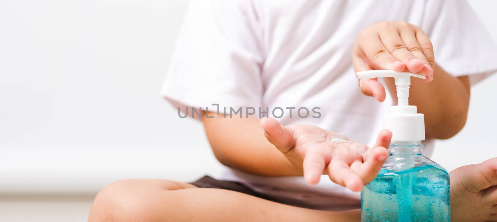 Closeup Asian little child boy sitting applying bottle pump dispenser sanitizer alcohol gel cleaning washing hands yourself, COVID-19 or coronavirus protection concept, isolated on white background with copy space