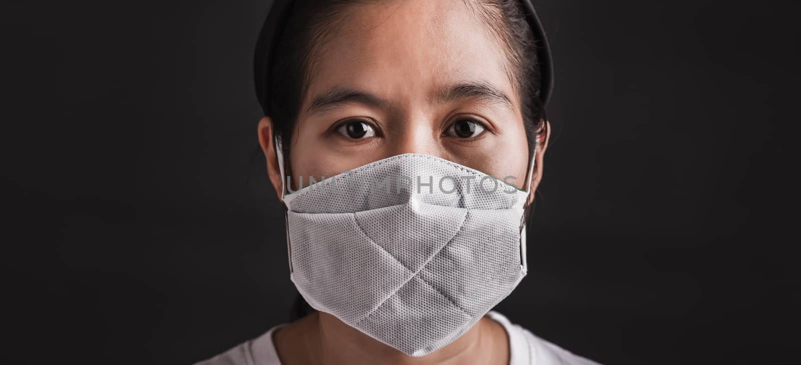 Closeup Asian young woman wearing protective face mask with fear in the eye, prevent germs or disease hygiene prevention COVID-19 virus or coronavirus protection concept, dark on black background