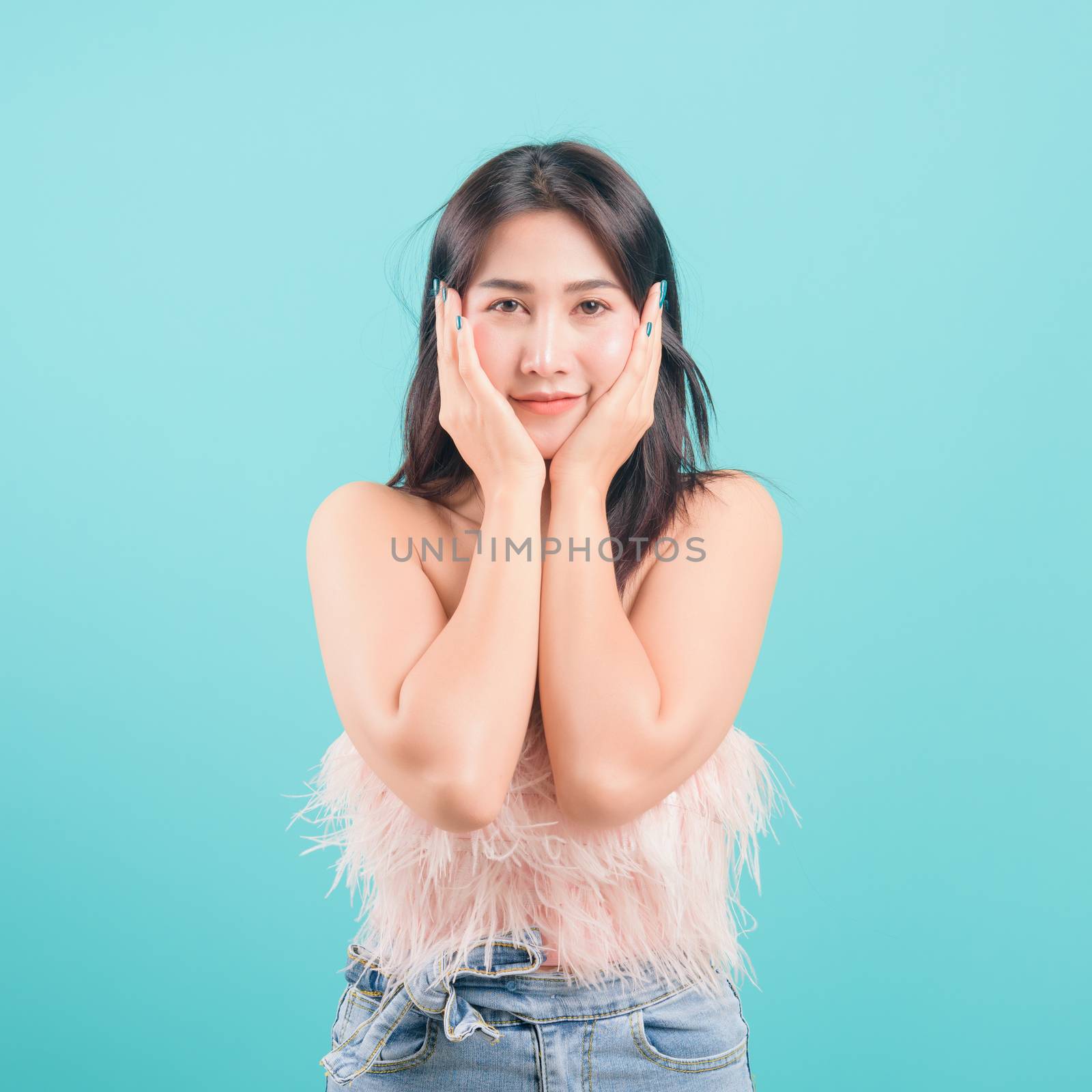 Asian happy portrait beautiful young woman standing smiling surprised excited her hands over her face and looking to camera on blue background with banner copy space for text