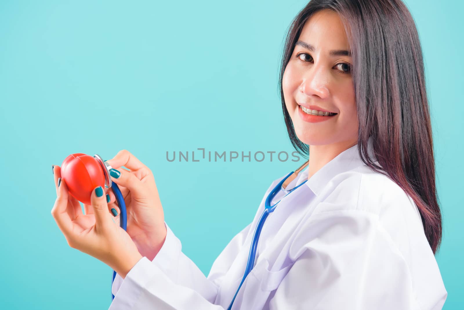 Portrait asian beautiful doctor woman smiling her standing with stethoscope examining red heart on blue background, with copy space for text