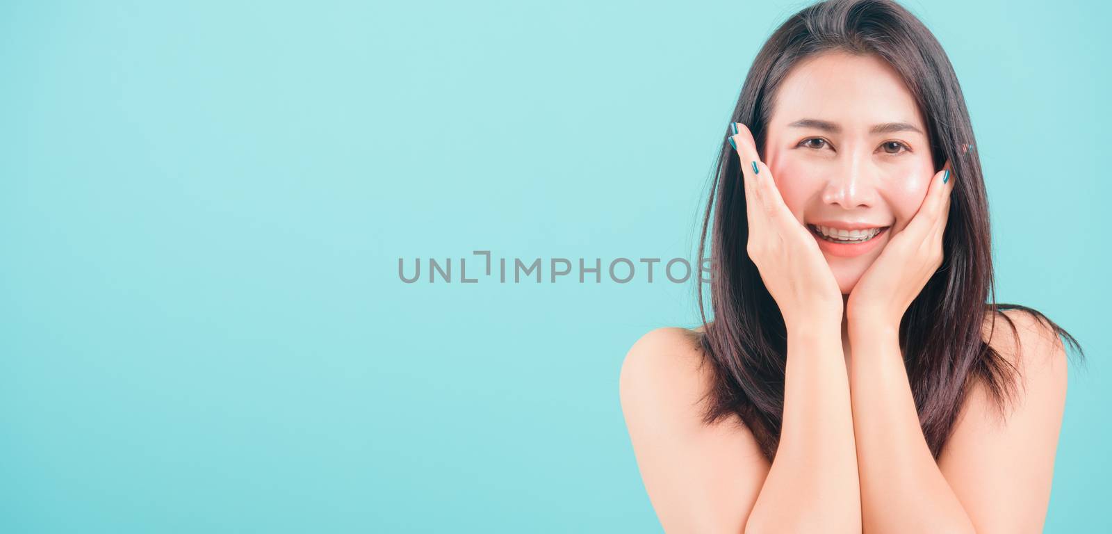 Asian happy portrait beautiful young woman standing smiling surprised excited her hands over her face and looking to camera on blue background with banner copy space for text