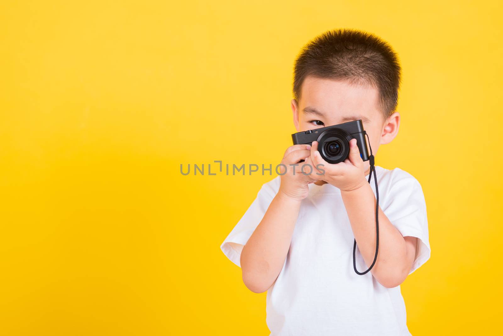 Asian Thai happy portrait cute little cheerful child boy hold photo camera compact doing taking the picture, studio shot isolated on yellow background with copy space