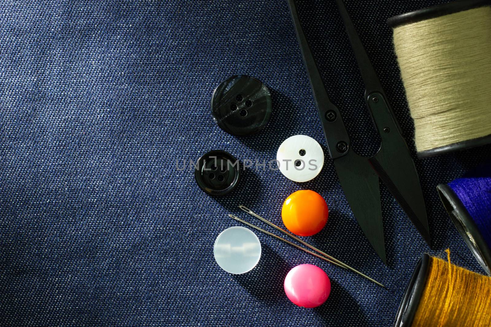 Needle and threads against plastic button and thread cutting scissors on jeans fabric. Top view and copy space for text. Concept of tailor or Designer.