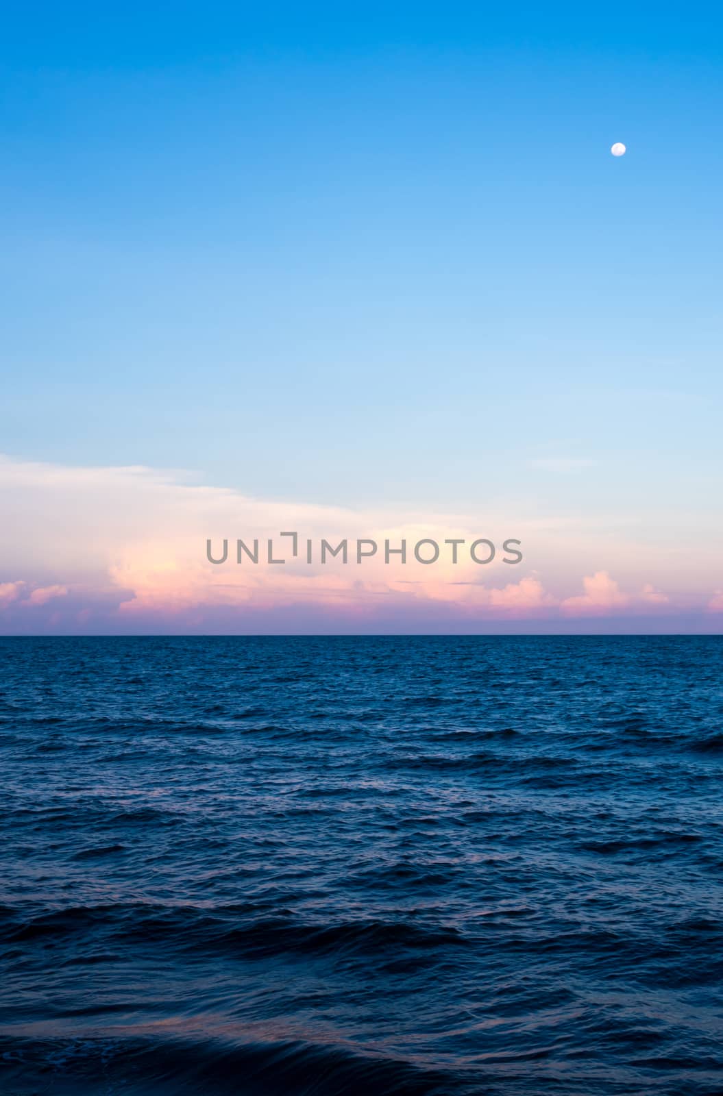 Pink Clouds and moon in sunset sky over sea