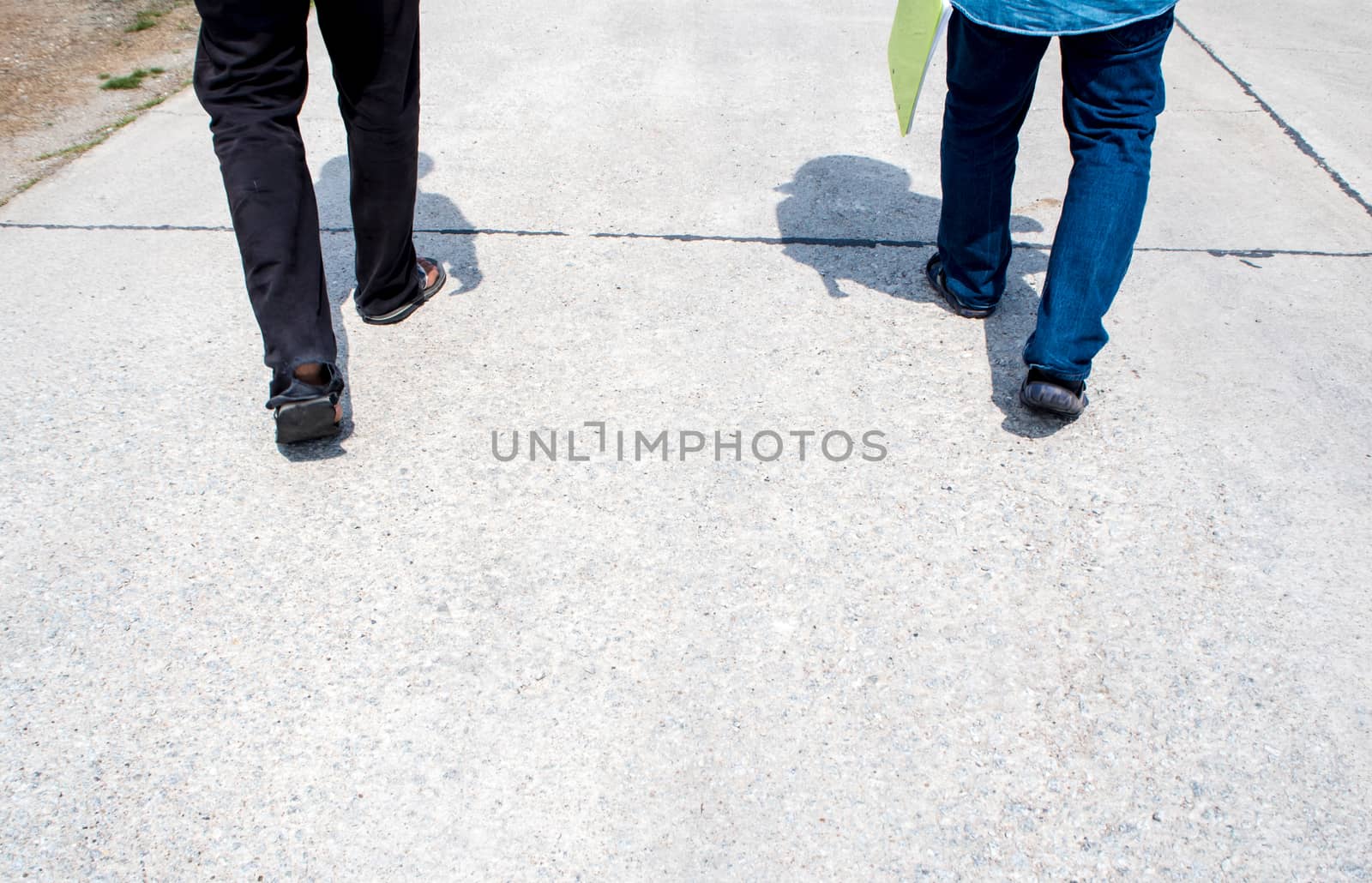 The legs of two men are walking together on a concrete walkway by Satakorn