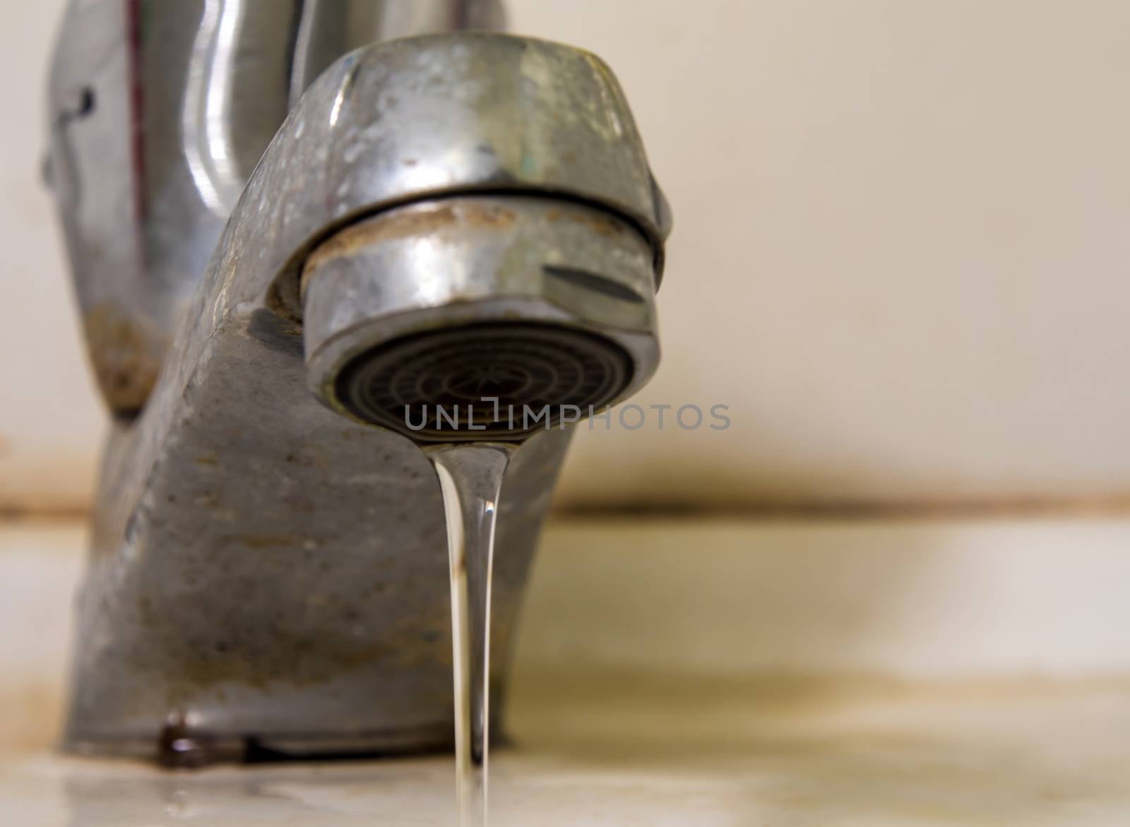 Leaking water drops from old rust and stained faucet by Satakorn