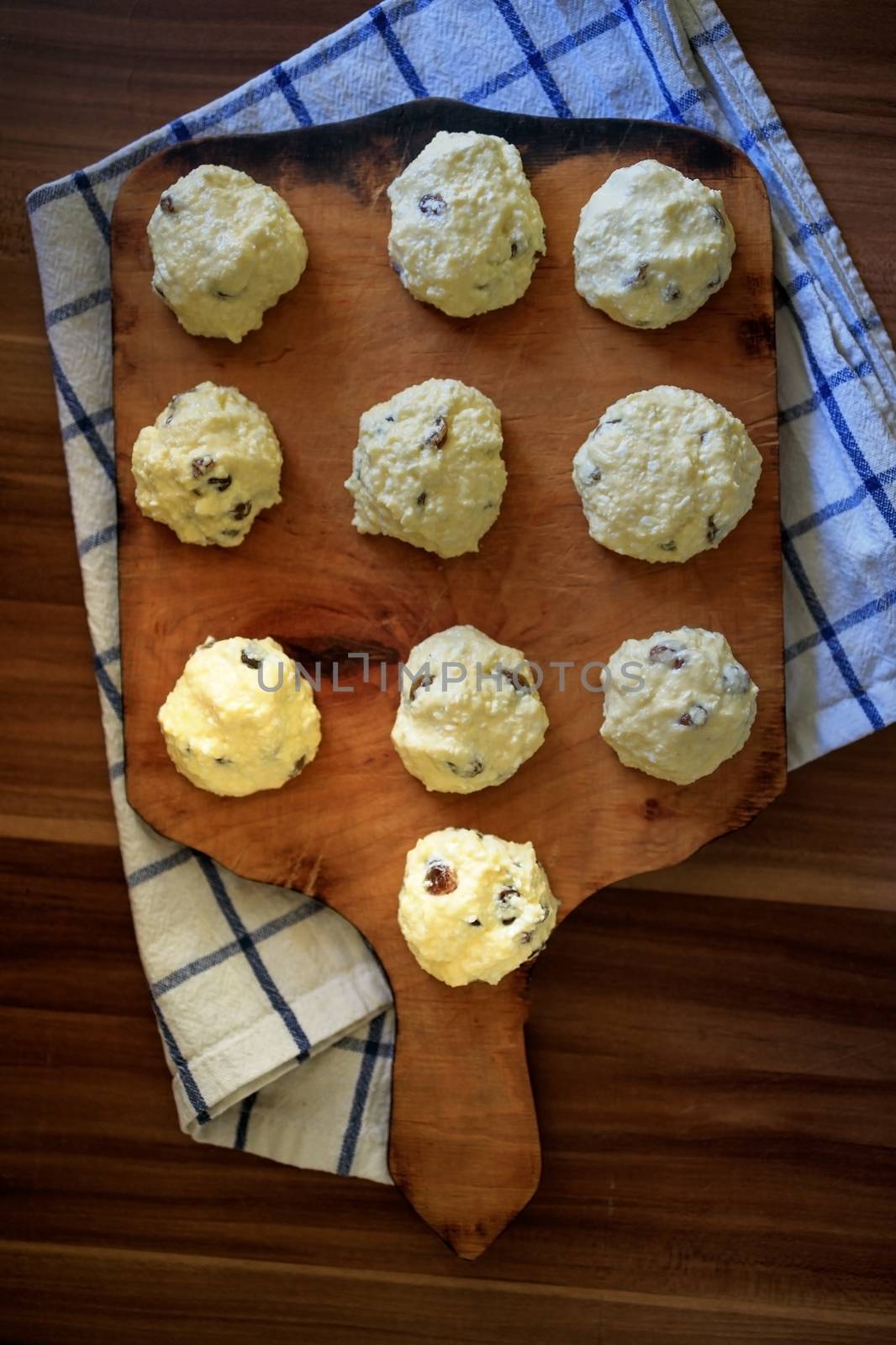 On the board prepared for frying Russian traditional home-made cottage cheese pancakes with raisins - cheesecakes on a wooden table.