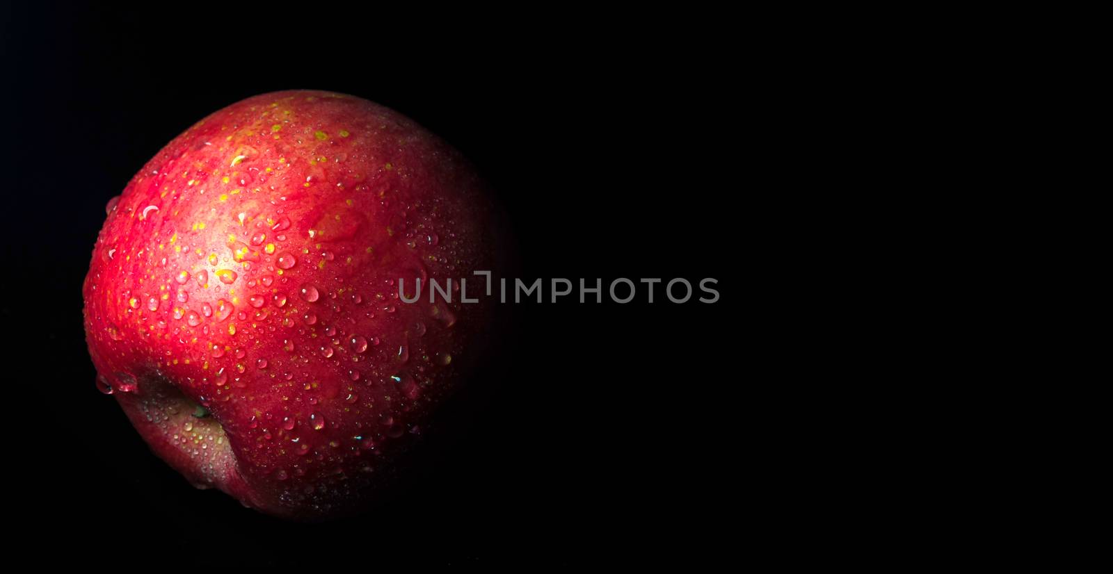 Water droplet on glossy surface of red apple on black background by Satakorn