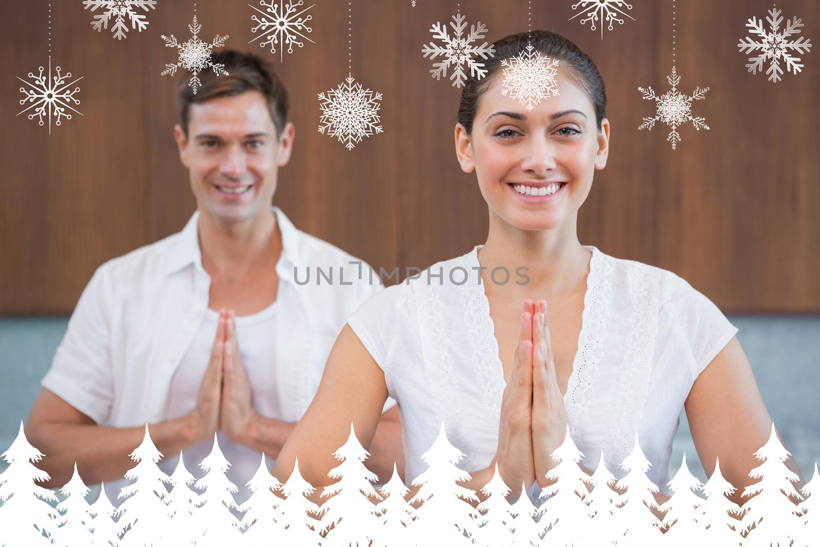 Smiling couple in white sitting in lotus pose with hands together against fir tree forest and snowflakes