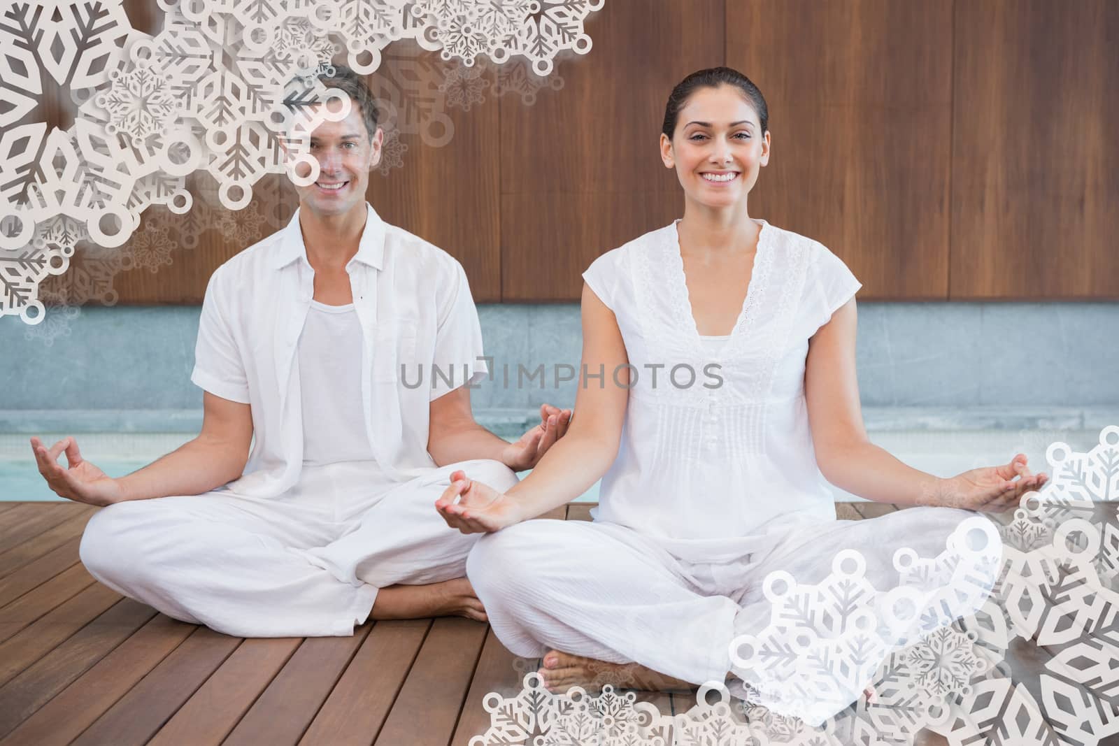 Attractive couple in white sitting in lotus pose smiling at camera against snowflake frame