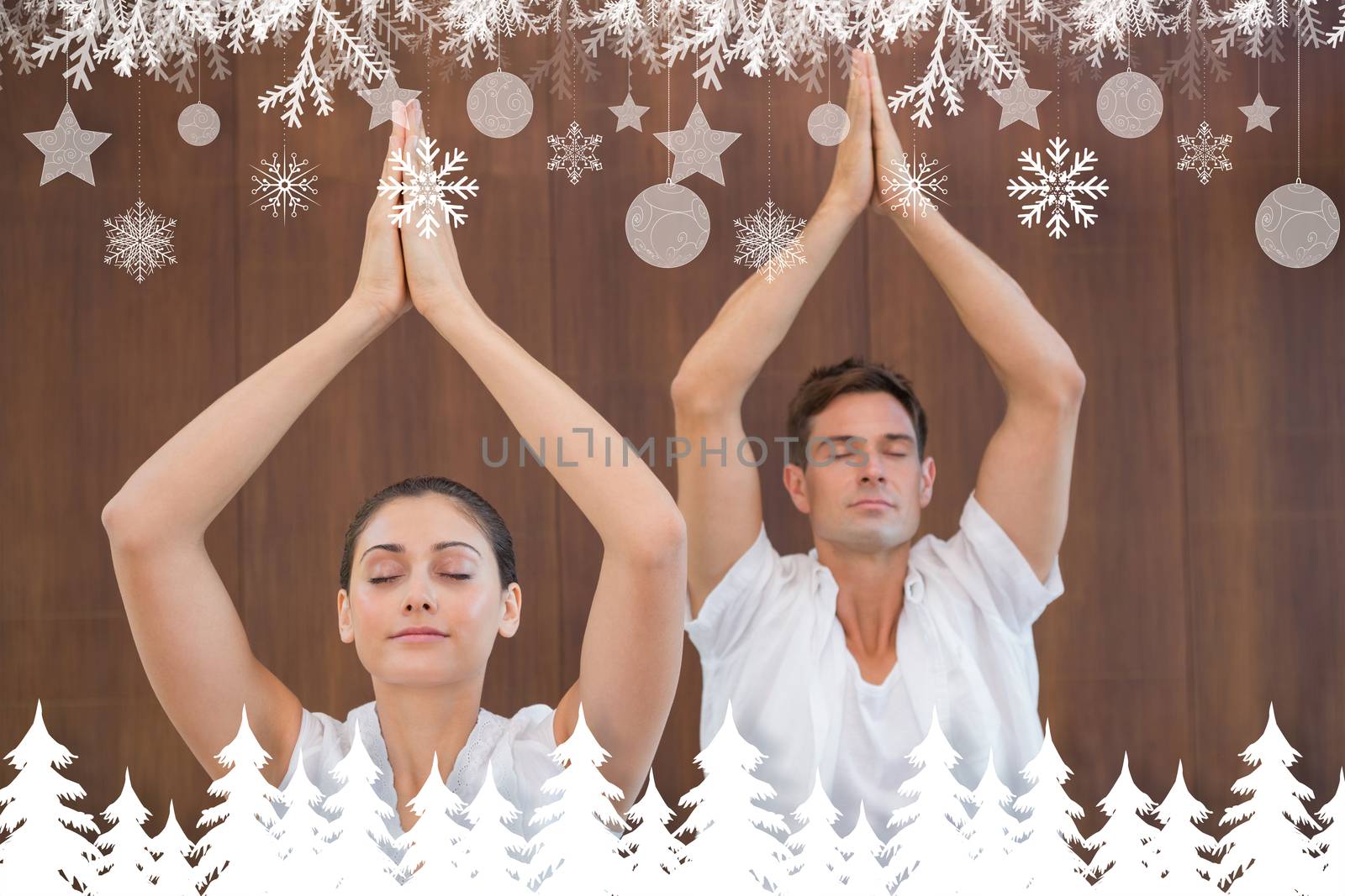 Peaceful couple in white doing yoga together with hands raised against fir tree forest and snowflakes