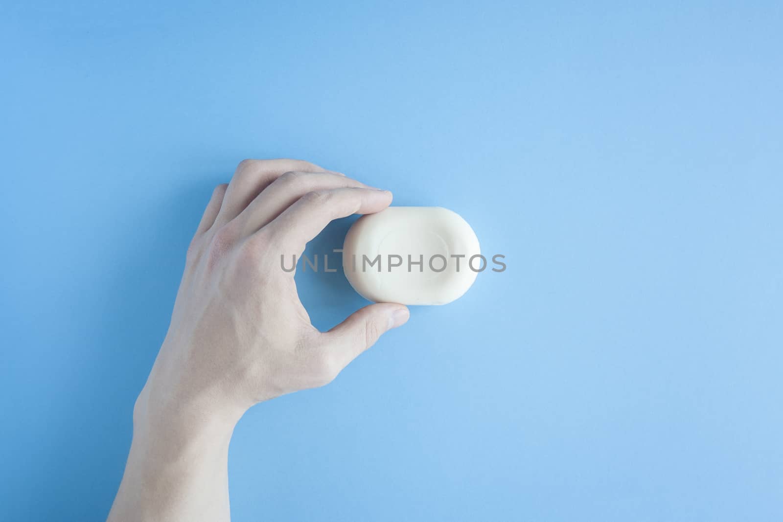 A piece of soap in a male hand a top view on a blue background. The human hand holds soap. Wash your hands. Soap against bacteria and viruses. Compliance with hygiene and sterility to combat coronavirus.