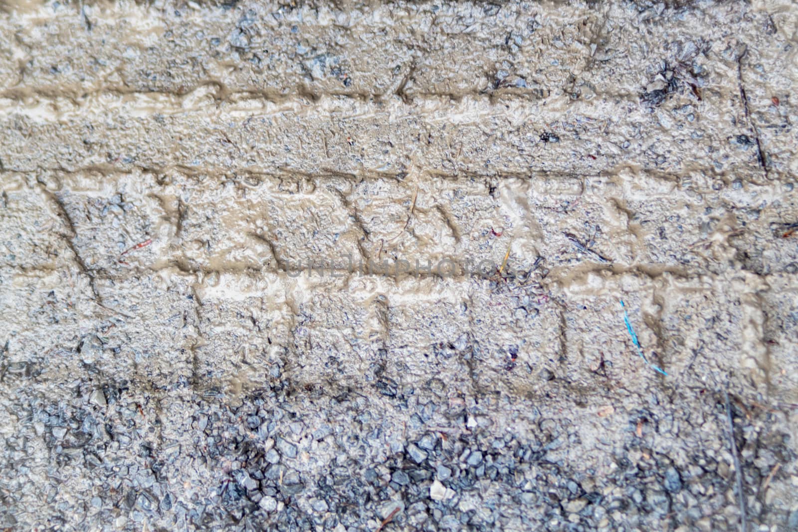 In a rural parking area filled with small gravel, tire tracks are seen impressed in the mud on a wet day.