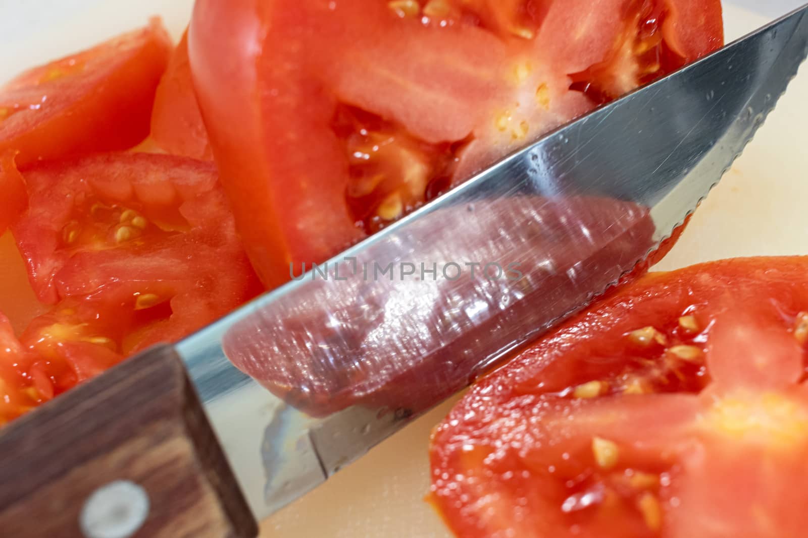 Close-up view of a steak knife with a wooden handle slicing through a red beefsteak tomato on a cutting board.
