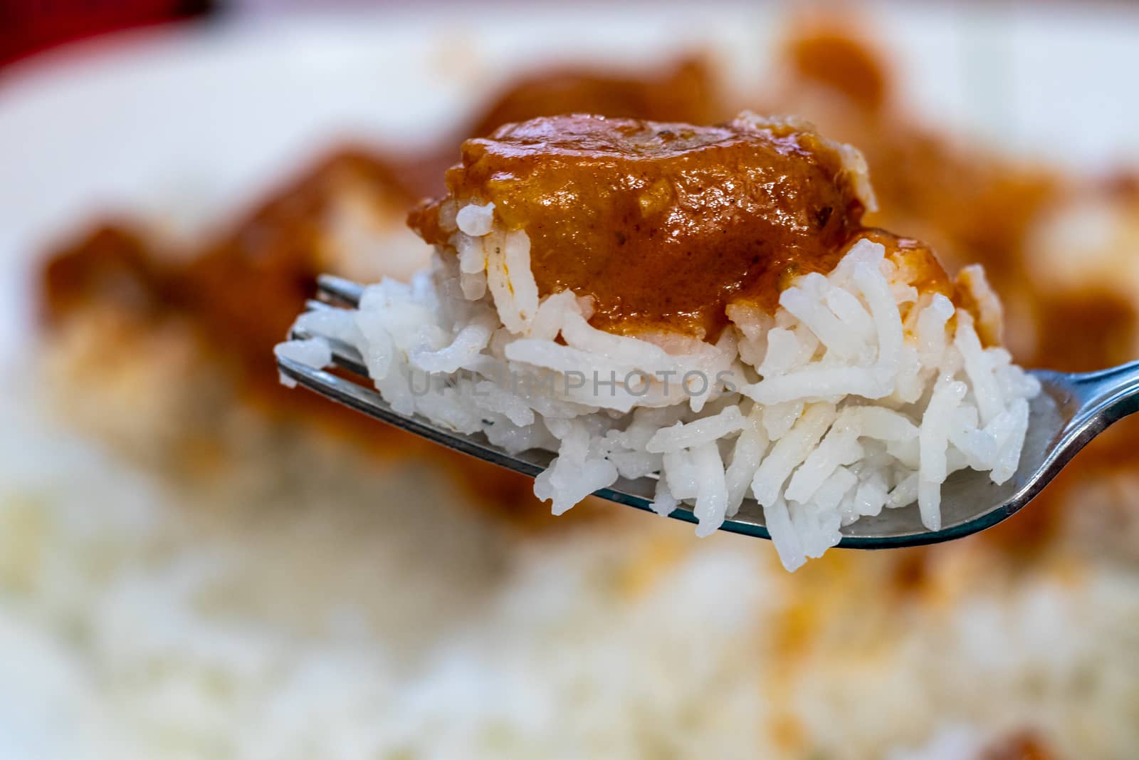 A piece of simulated (vegetarian) chicken in a butter chicken dish sits on a scoop of white basmati rice on a fork.