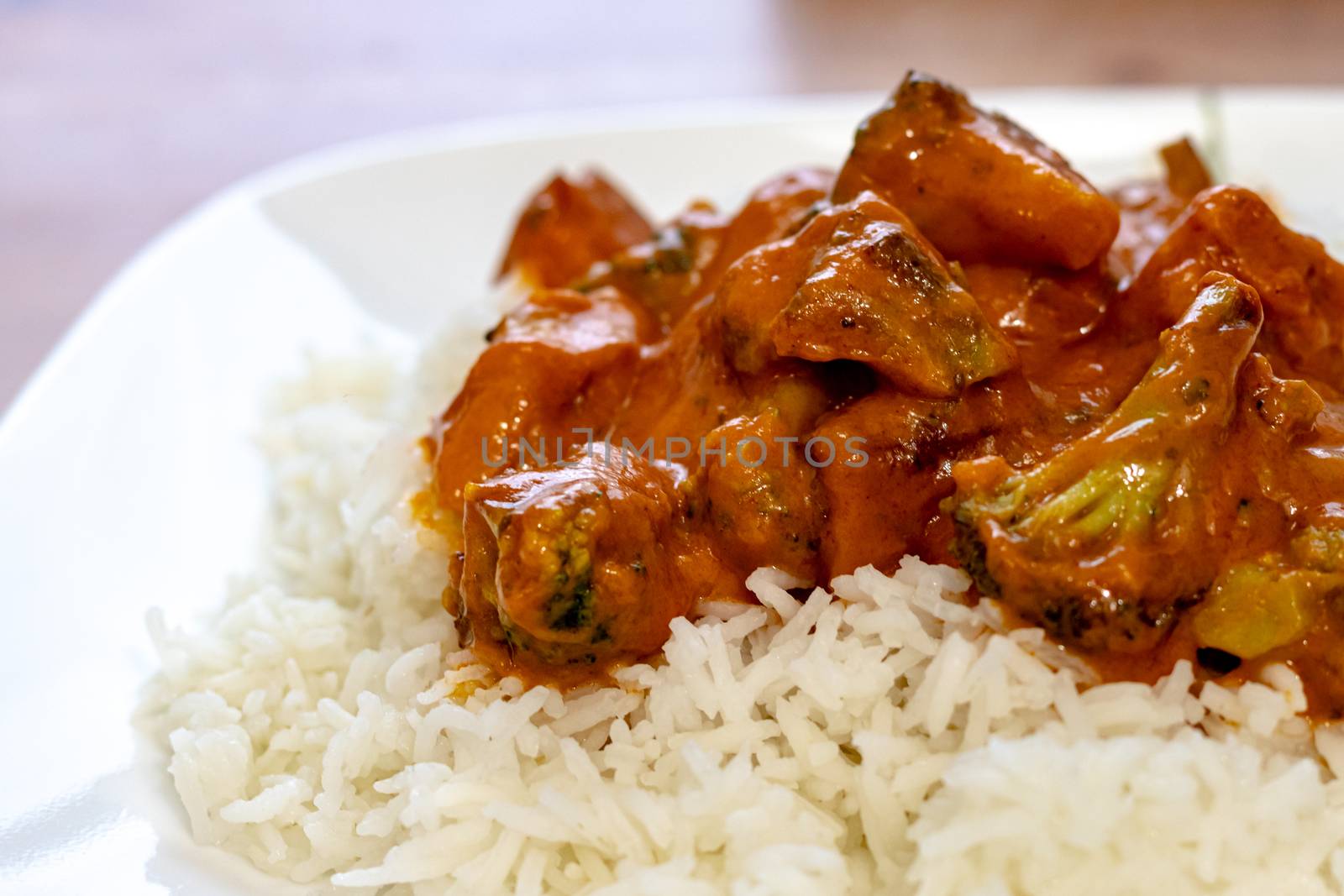 A vegetarian dish of broccoli and simulated chicken is served up with a butter chicken tomato sauce from Indian cuisine on a bed of basmati rice.