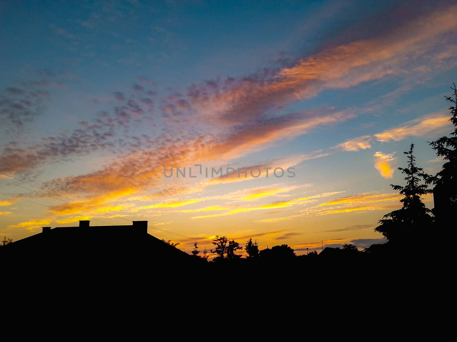 Cloudy colorful sunset over silhouettes of building and trees 