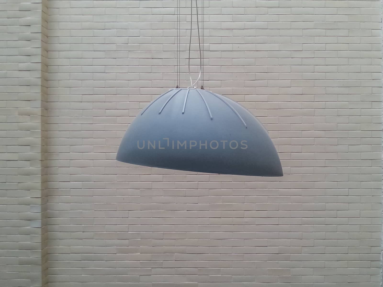 Gray huge lamp in front of white brick wall by Wierzchu