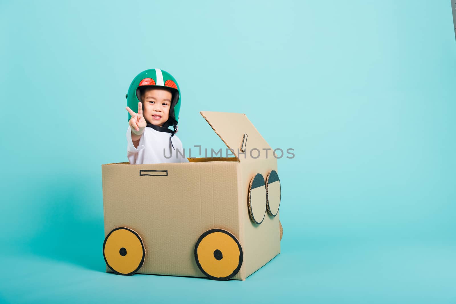 Happy Asian children boy with Helmet smile in driving play car creative by a cardboard box imagination, summer holiday travel concept, studio shot on blue background with copy space for text