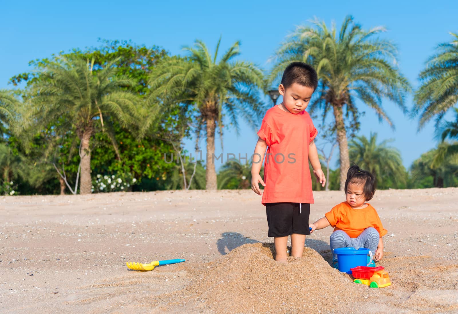 Asian Thai happy cute little cheerful Brother and sister two children funny digging play toy with sand at an outdoor tropical beach in summer day with copy space