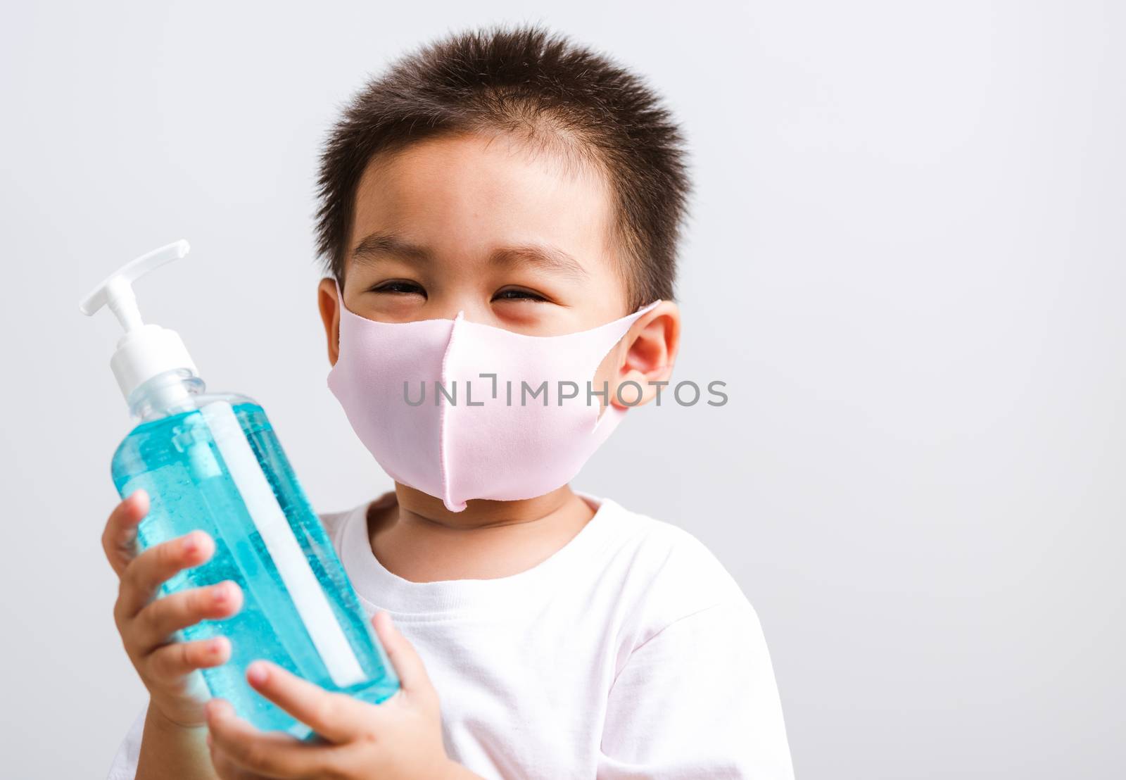Closeup portrait Asian little child boy holding show bottle pump dispenser sanitizer alcohol gel hand wash cleaning, COVID-19 or coronavirus protection concept, isolated on white background