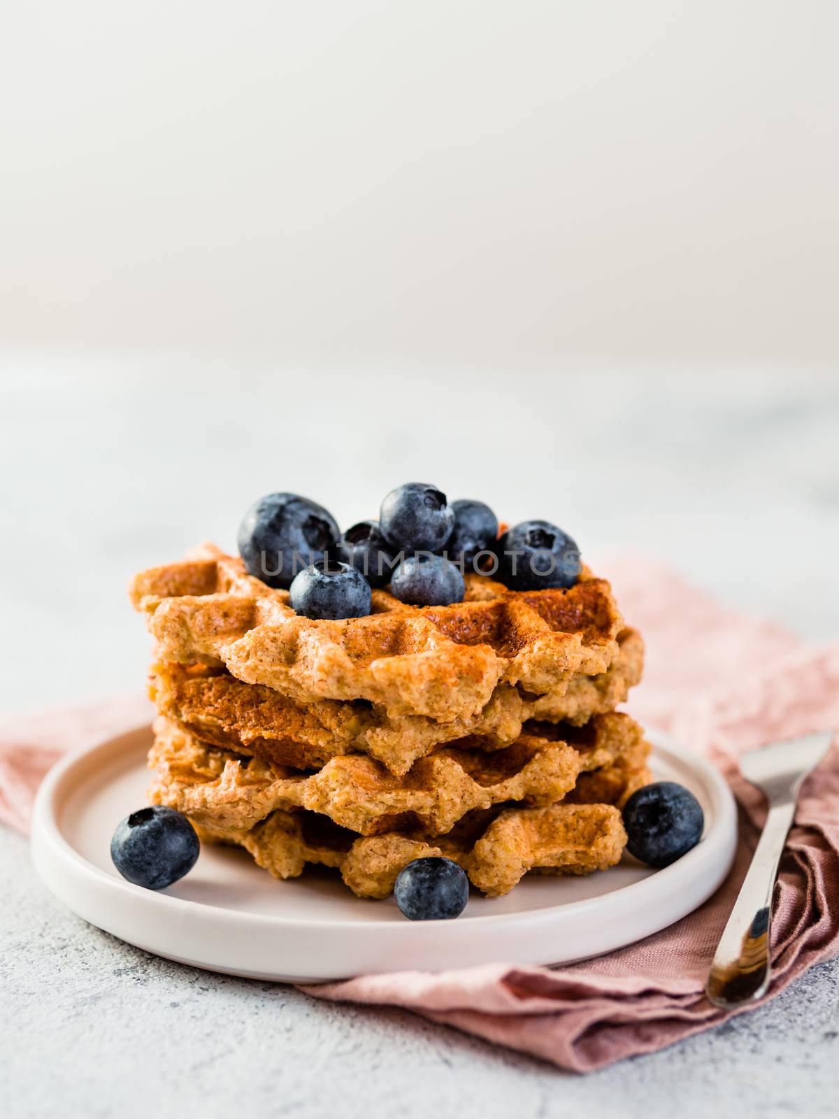 Easy healthy gluten free oat waffles with copy space. Stack of appetizing homemade waffles with oat flour decorated blueberries, on plate over light gray cement background. Vertical