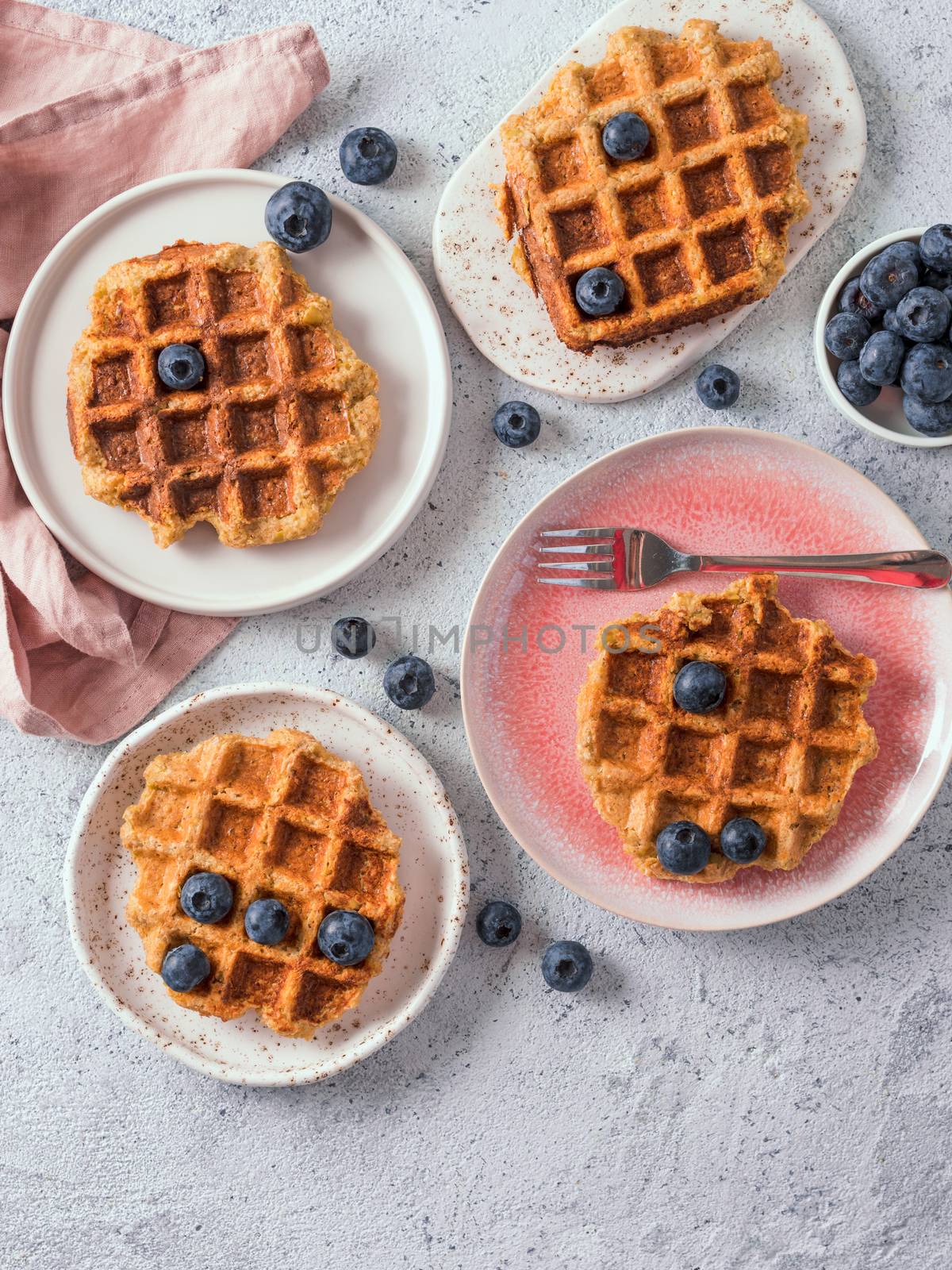 Easy healthy gluten free oat waffles with copy space. Plates with appetizing homemade waffles with oat flour decorated blueberries, on light gray cement background. Vertical. Top down view or flat lay