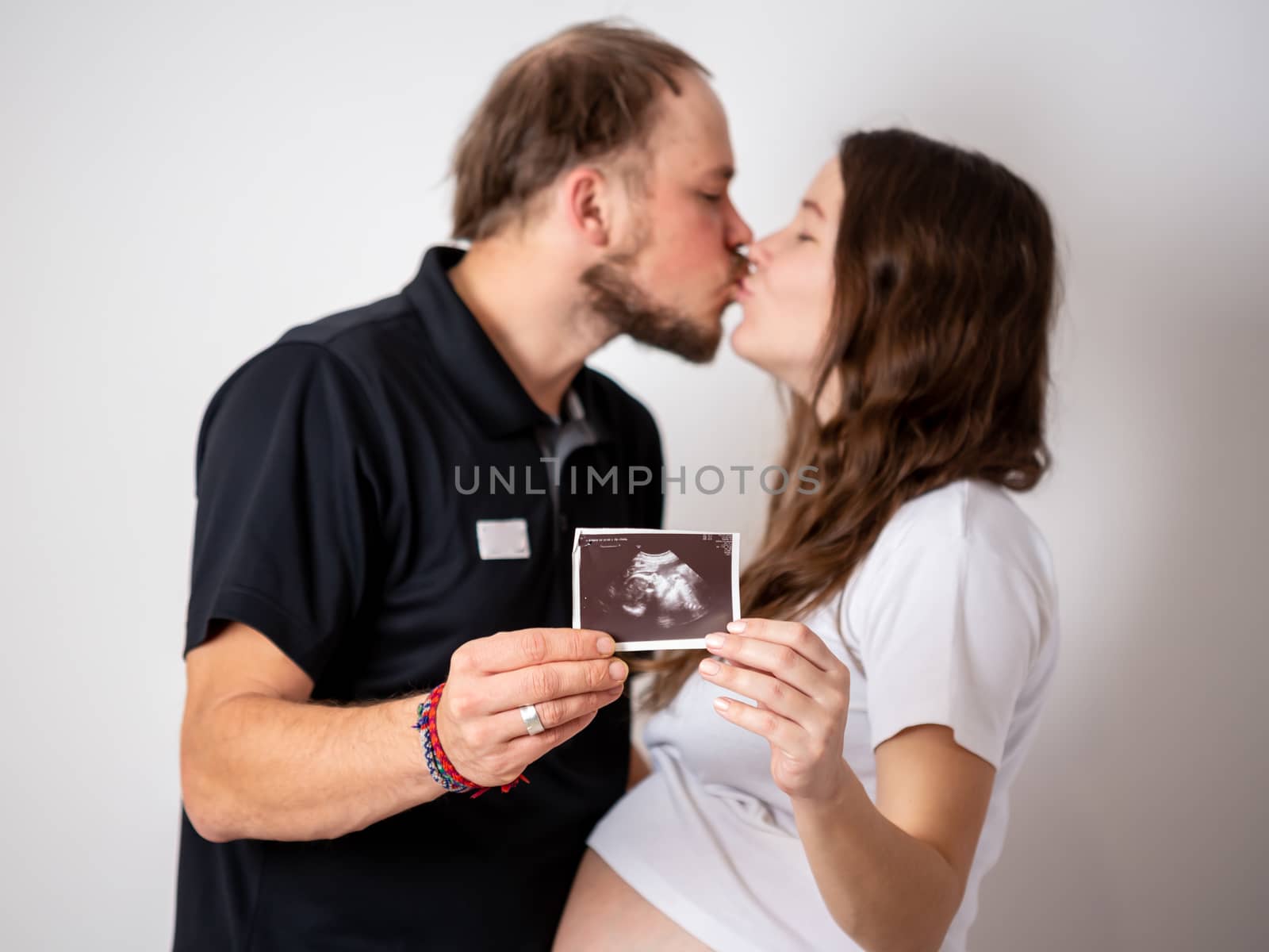 Happy married couple are showing pregnancy test stick and ultrasound picture of their unborn baby. Focus on two stripes.