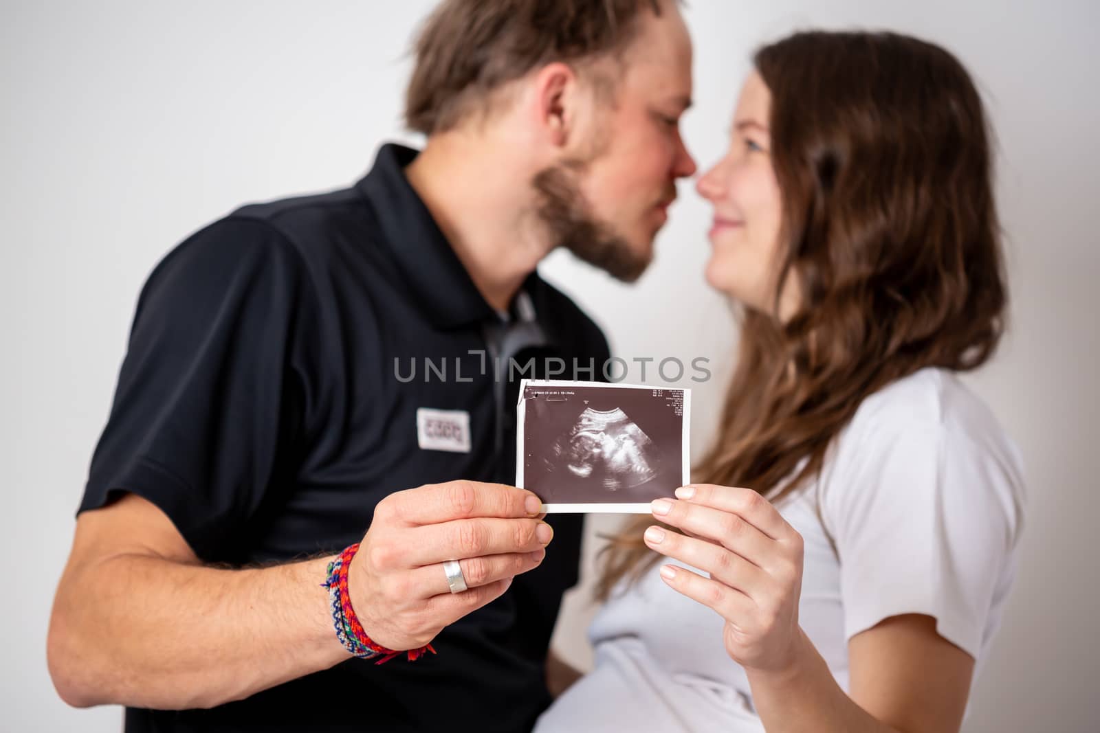 Happy married couple are showing pregnancy test stick and ultrasound picture of their unborn baby. Focus on two stripes by Vassiliy