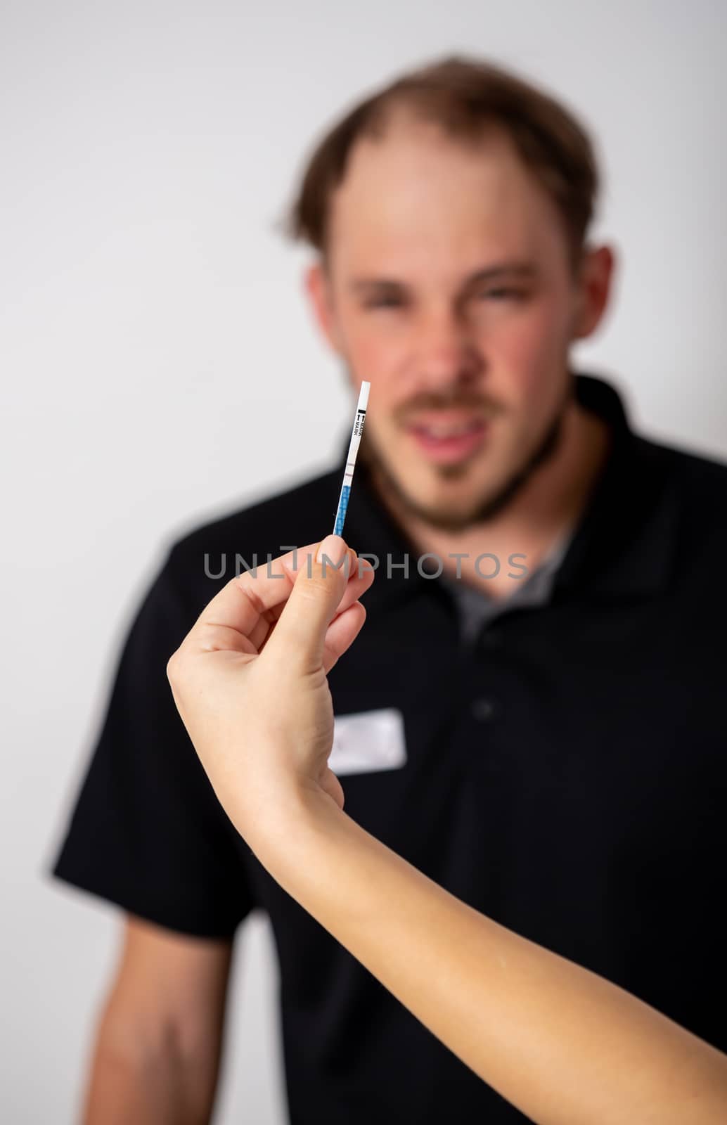 Positive pregnancy test held by a surprised man in the background.