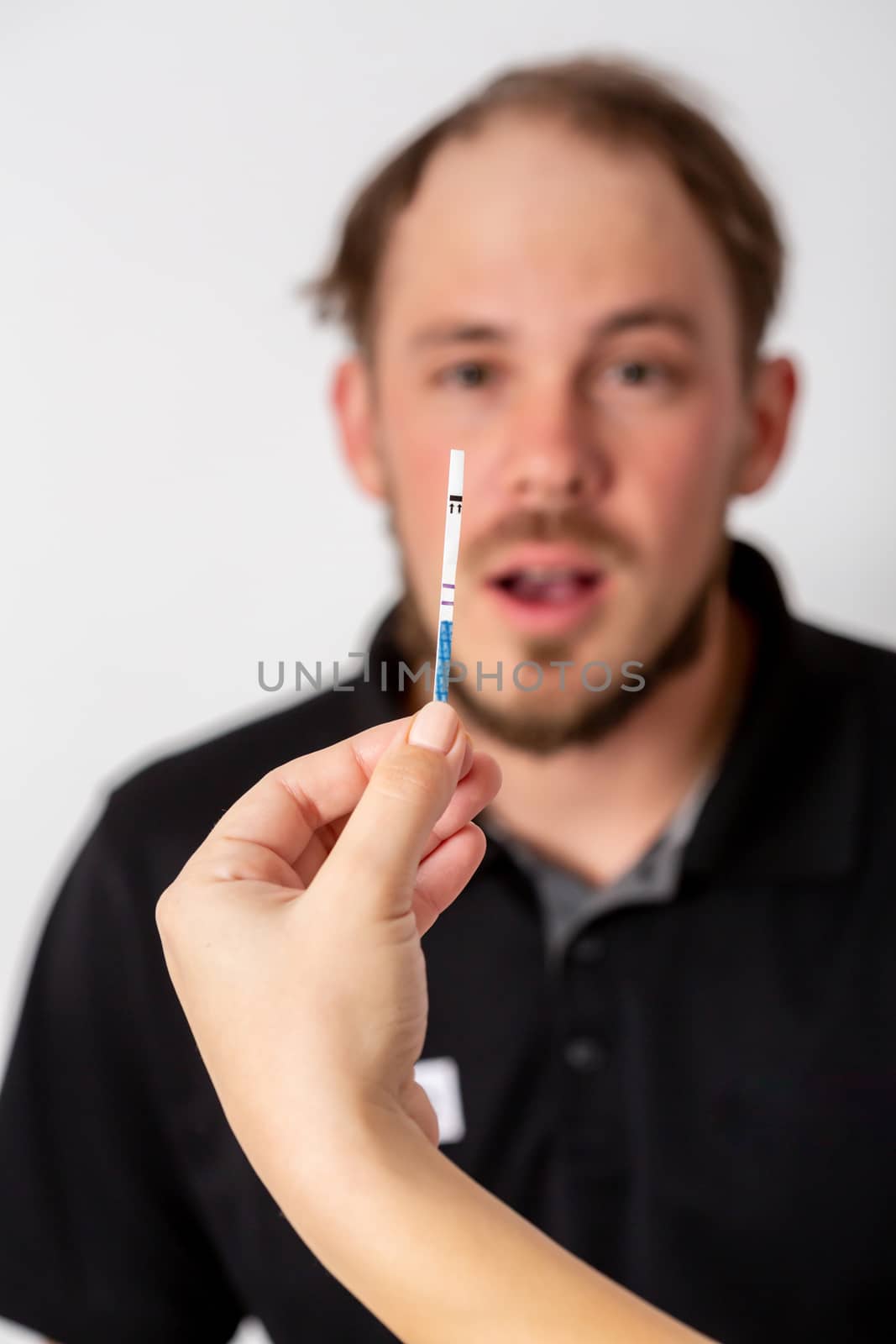 Positive pregnancy test held by a surprised man in the background.