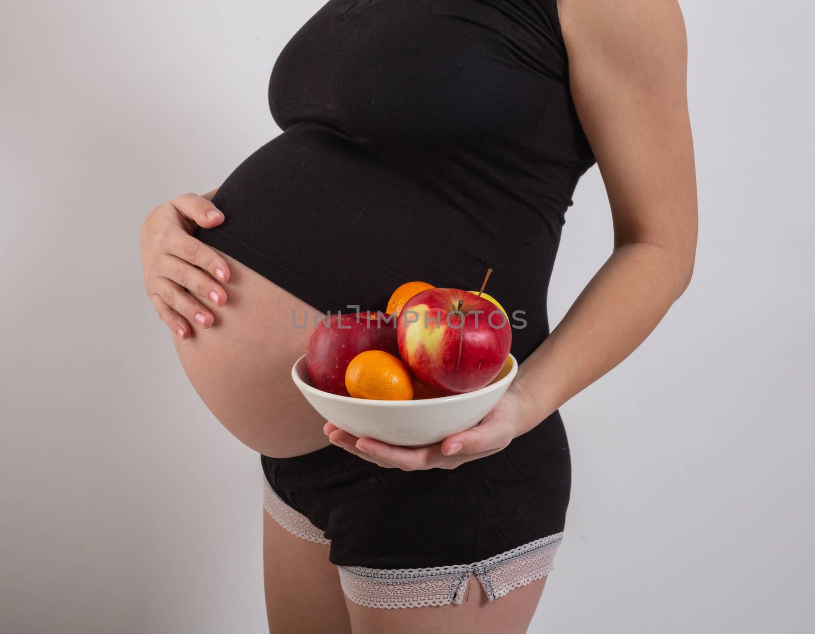 Pregnancy and healthy organic nutrition. Pregnant woman holds fresh vitamin fruits, free space. Place for text. Concept of expectation and health