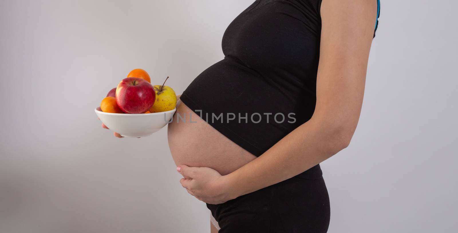 Pregnancy and healthy organic nutrition. Pregnant woman holds fresh vitamin fruits, free space. Place for text. Concept of expectation and health