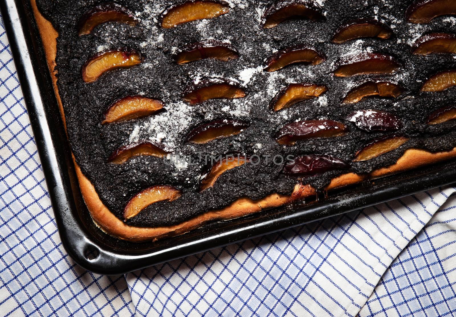 food background plum poppy seed cake on black pan