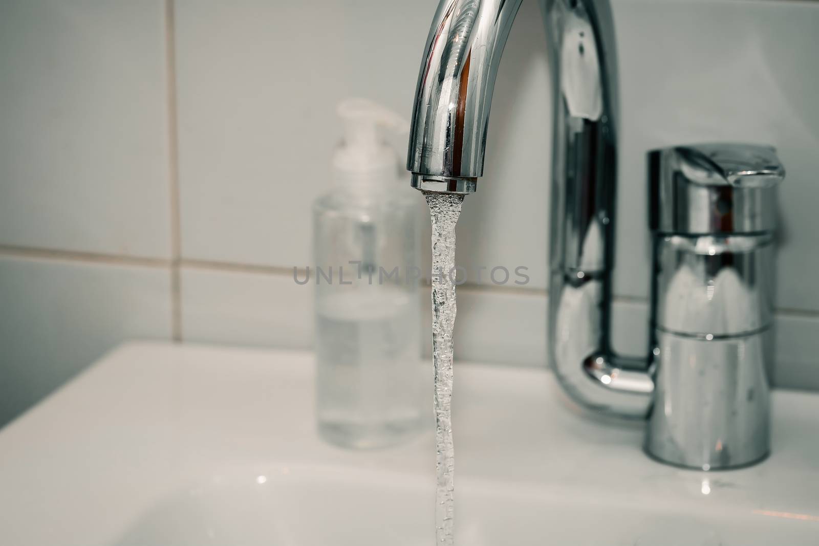 Modern hand wash basin. Solid tabletop surface and gray tile wall. Dispensable soap next to water tap on bathroom sink